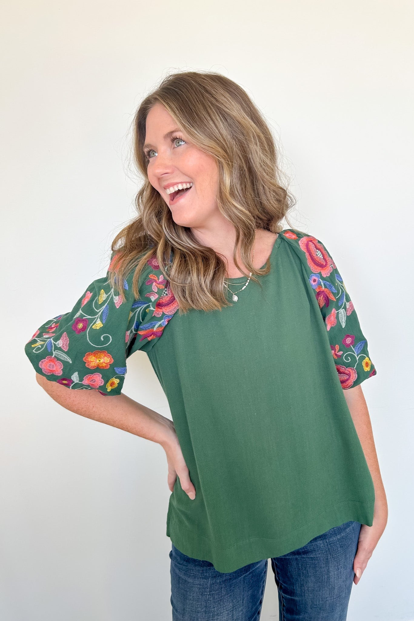 Woman wearing a green top with floral sleeves against a white background