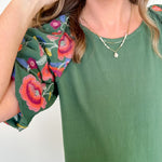 Woman wearing a green top with colorful floral sleeves against a white background