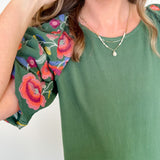 Woman wearing a green top with colorful floral sleeves against a white background