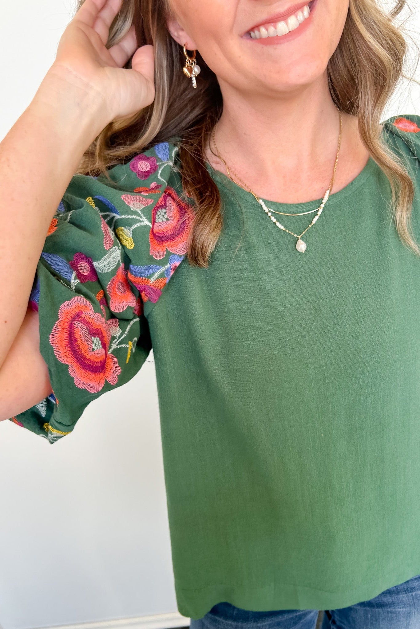 Woman wearing a green top with colorful floral sleeves against a white background