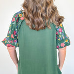 Person wearing a green top with floral sleeves against a white background