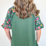 Person wearing a green top with floral sleeves against a white background
