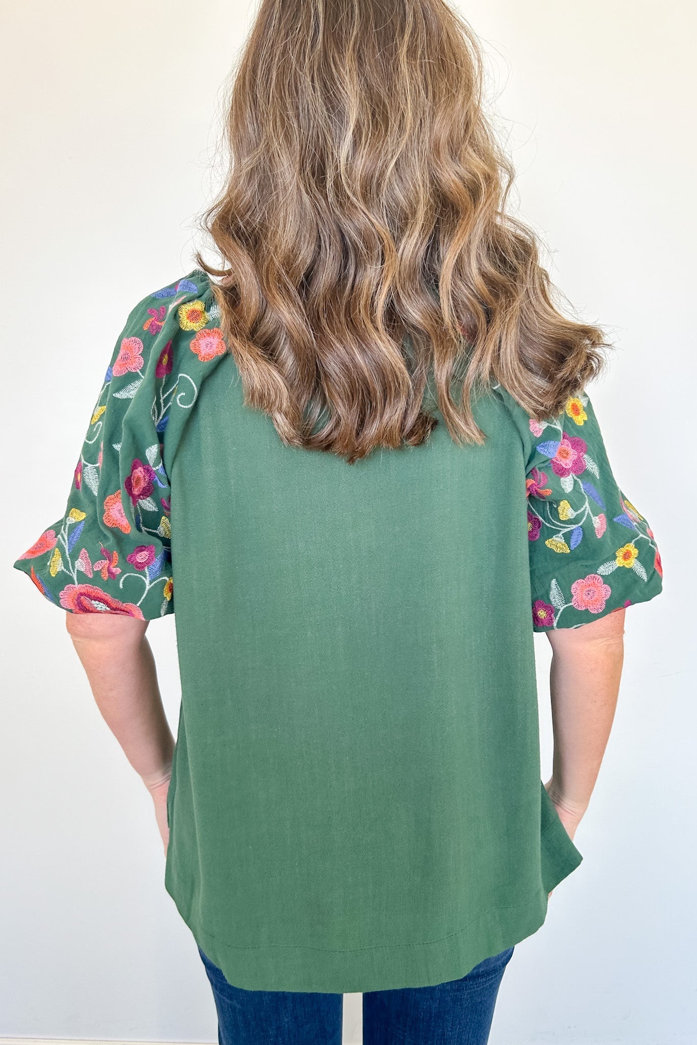 Person wearing a green top with floral sleeves against a white background