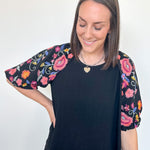Woman wearing a black top with colorful floral sleeves against a white background