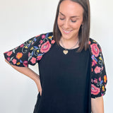 Woman wearing a black top with colorful floral sleeves against a white background