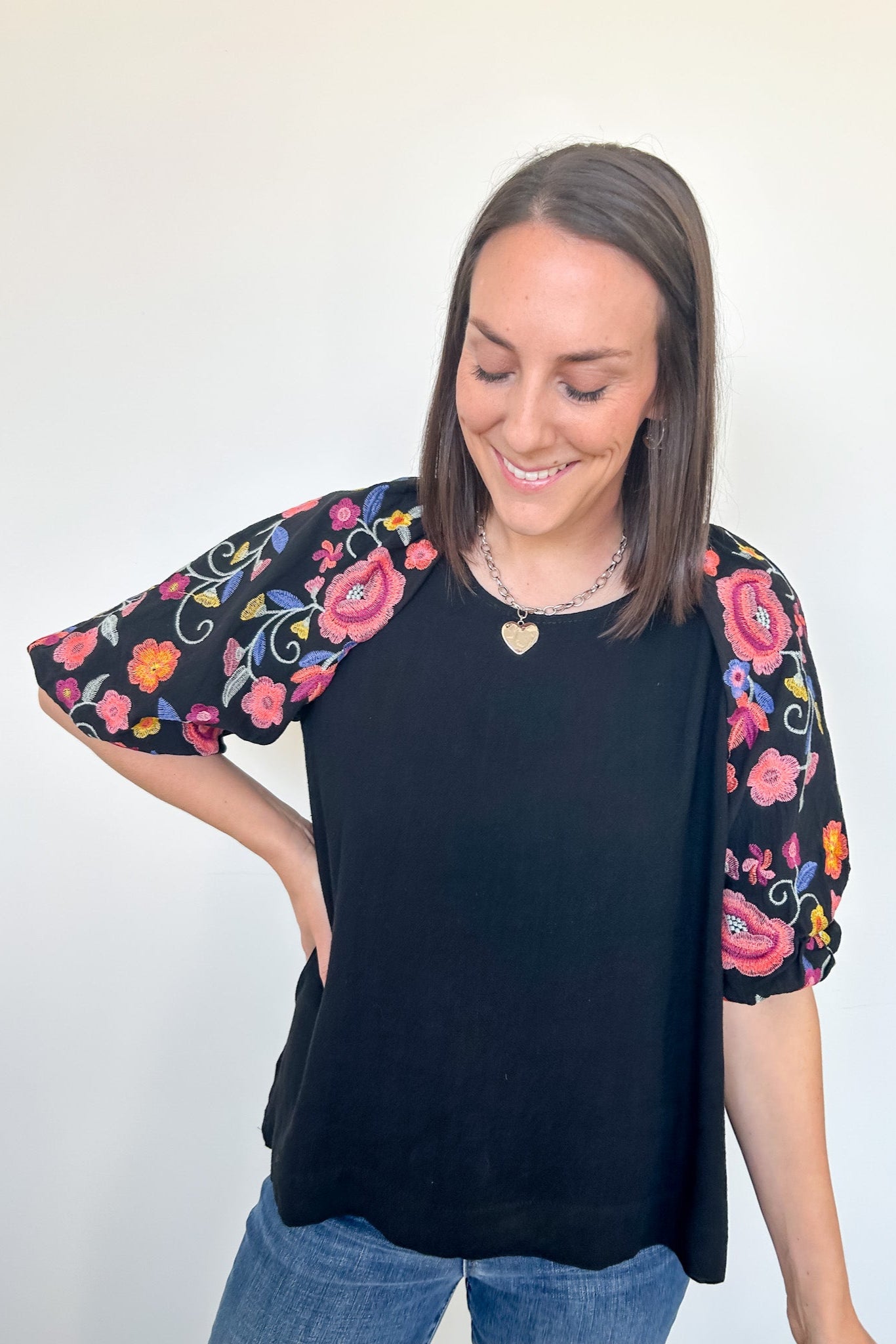 Woman wearing a black top with colorful floral sleeves against a white background
