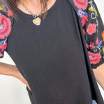 Black top with colorful floral embroidery on sleeves worn by a person.
