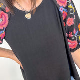 Black top with colorful floral embroidery on sleeves worn by a person.