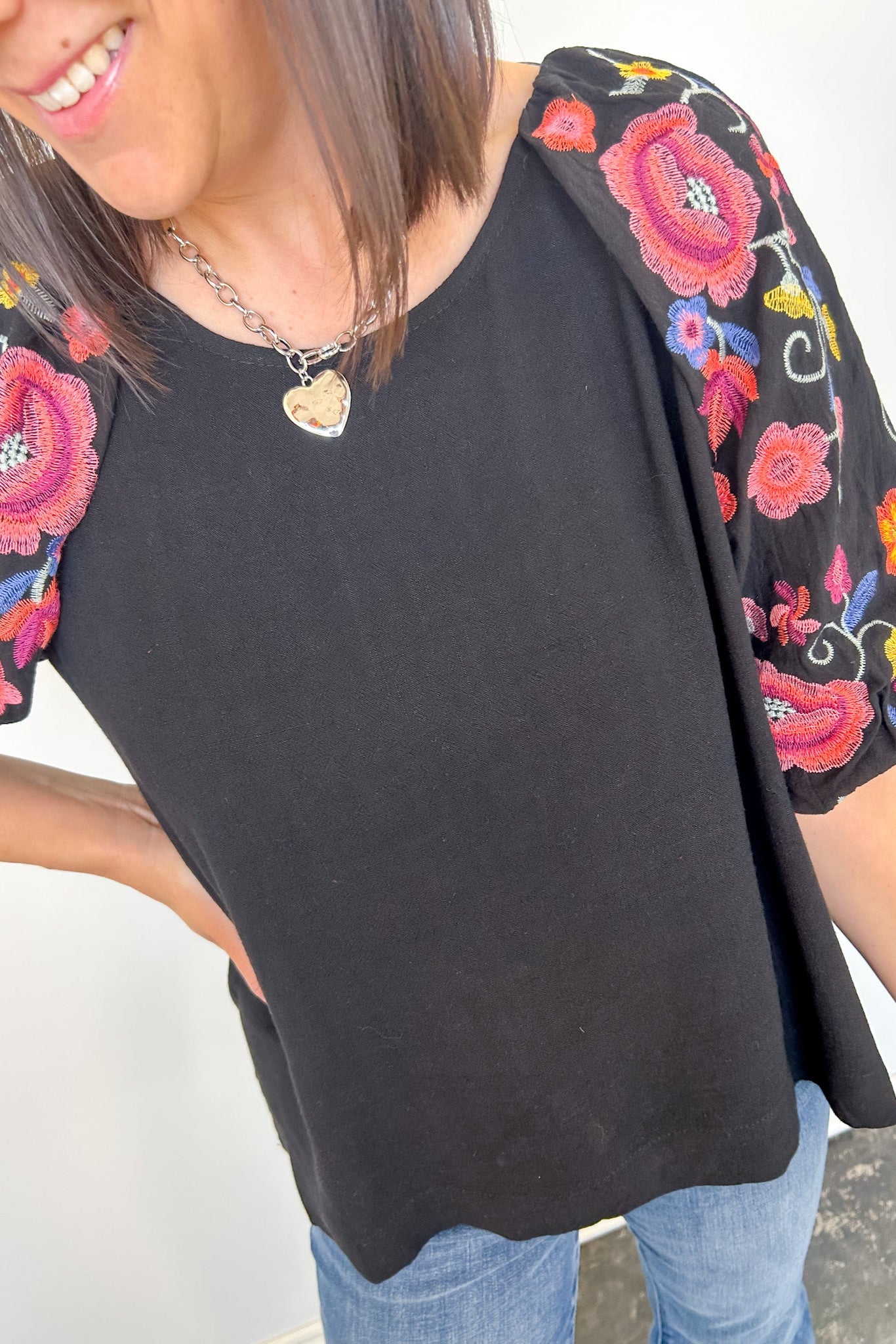 Black top with colorful floral embroidery on sleeves worn by a person.