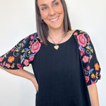 Woman wearing a black top with colorful floral sleeves against a white background