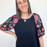 Woman wearing a black top with colorful floral sleeves against a white background
