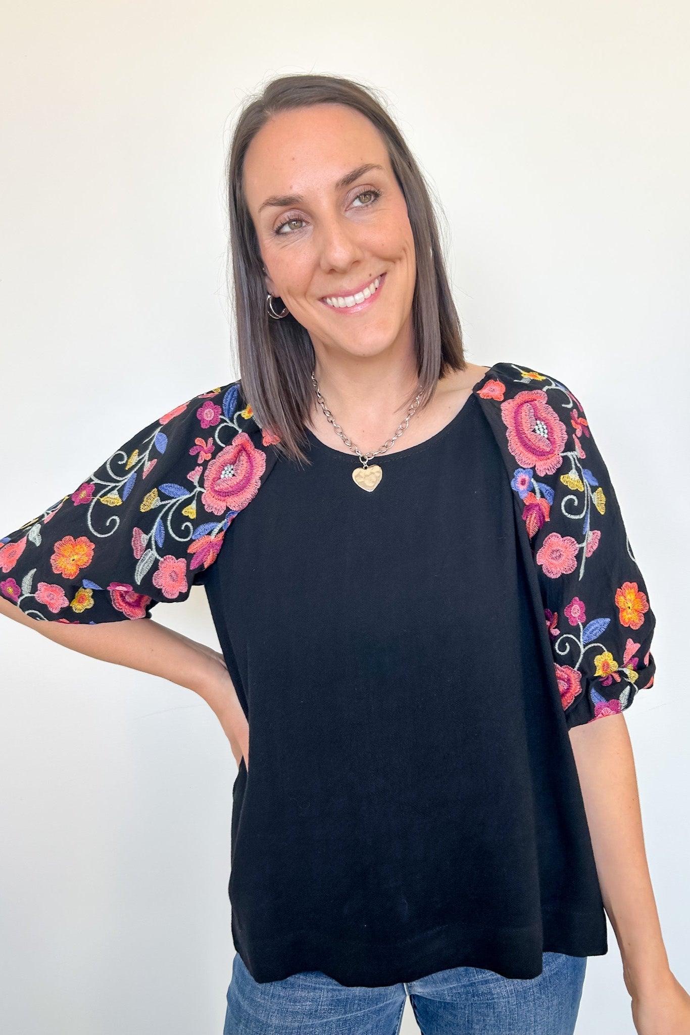 Woman wearing a black top with colorful floral sleeves against a white background