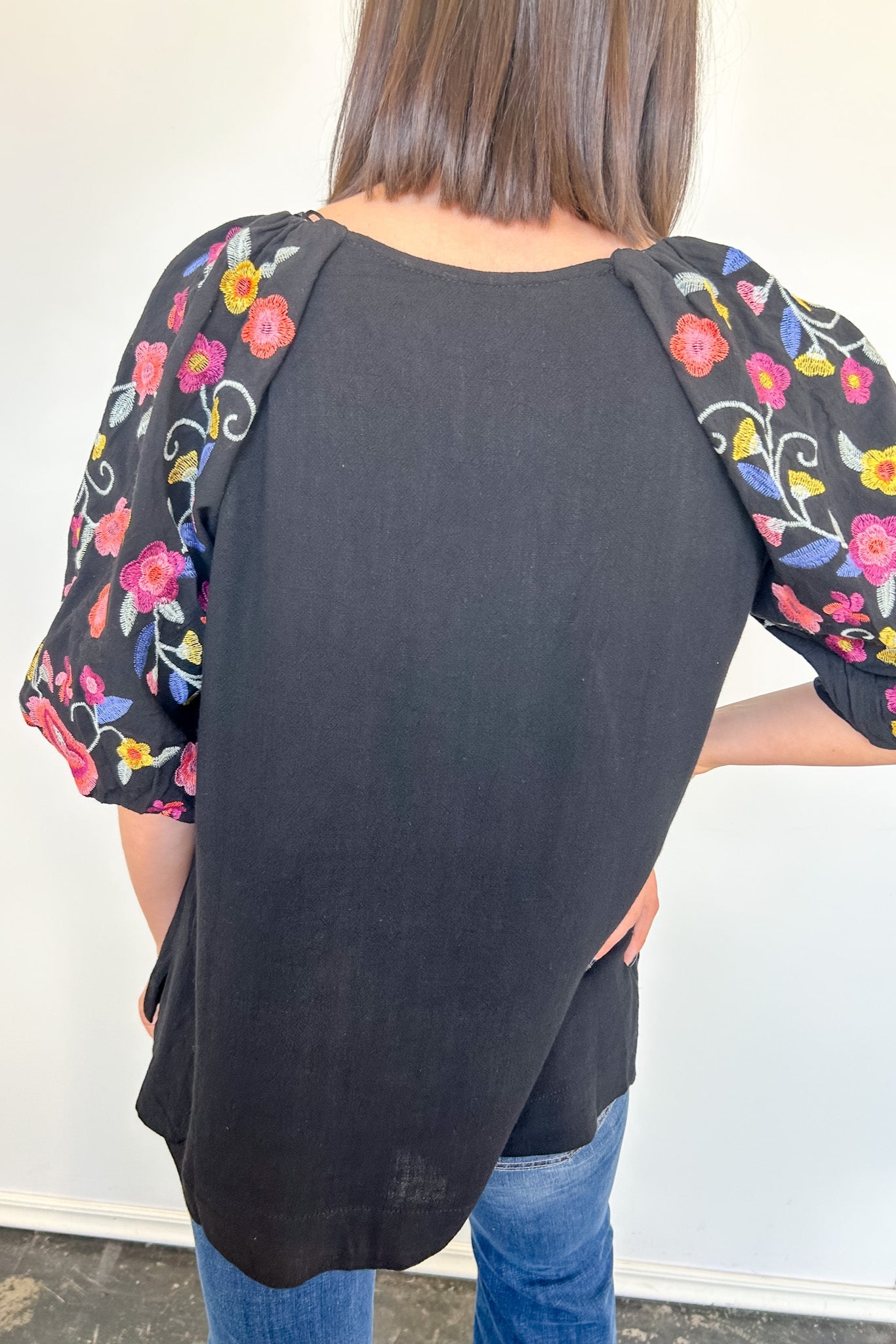 Black baseball-style shirt with floral sleeves worn by a person against a white wall.