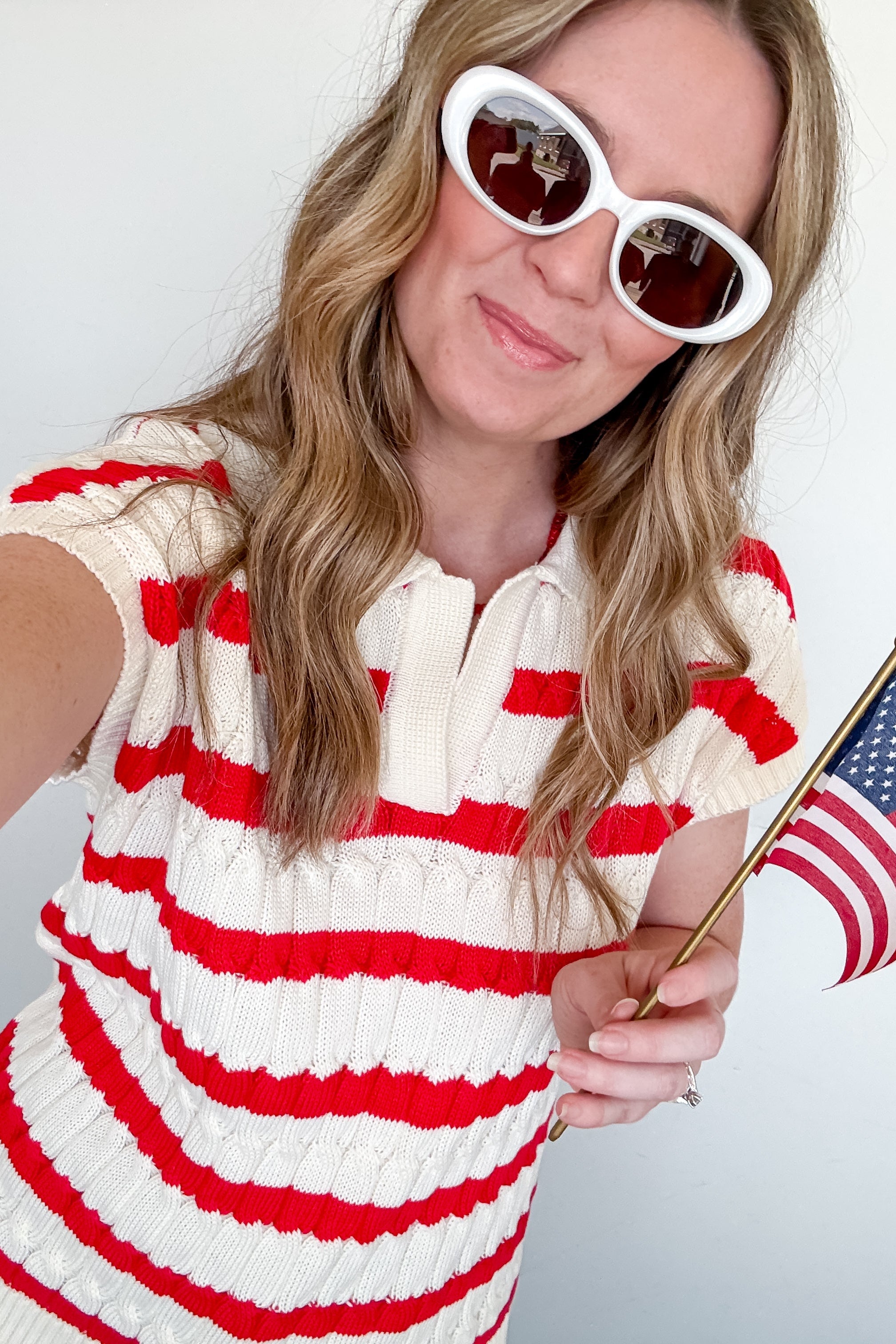 Woman wearing a red and white striped dress with sunglasses, holding an American flag.