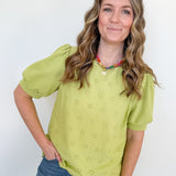 Woman wearing a green blouse with puff sleeves and blue jeans against a white background