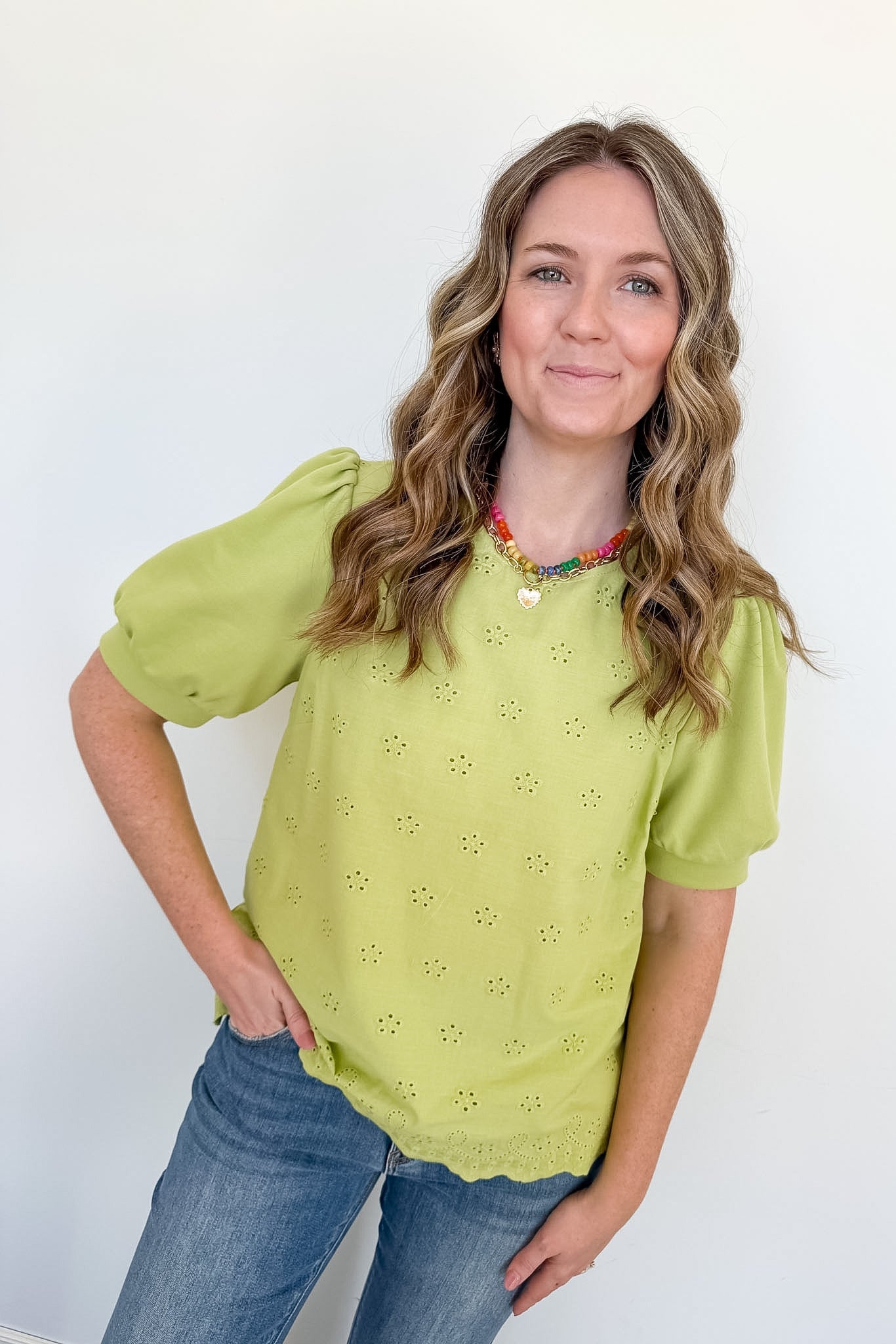 Woman wearing a green blouse with puff sleeves and blue jeans against a white background