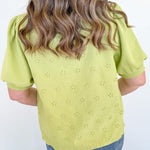 Person wearing a light green blouse with floral eyelet design and blue jeans against a white background