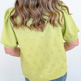 Person wearing a light green blouse with floral eyelet design and blue jeans against a white background