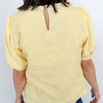 Person wearing a yellow blouse with floral patterns against a white background