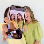 Person holding a phone with a photo of two women on the screen, with a plain background