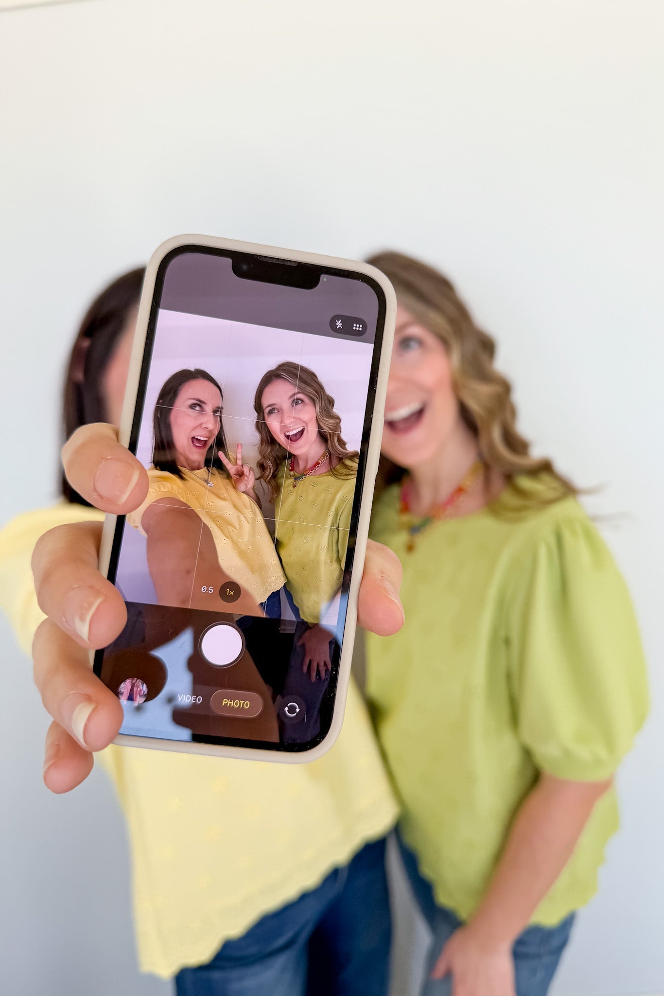 Person holding a phone with a photo of two women on the screen, with a plain background