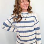 Woman in blue and white striped sweater standing against a white wall.