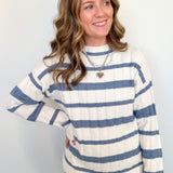 Woman in blue and white striped sweater standing against a white wall.