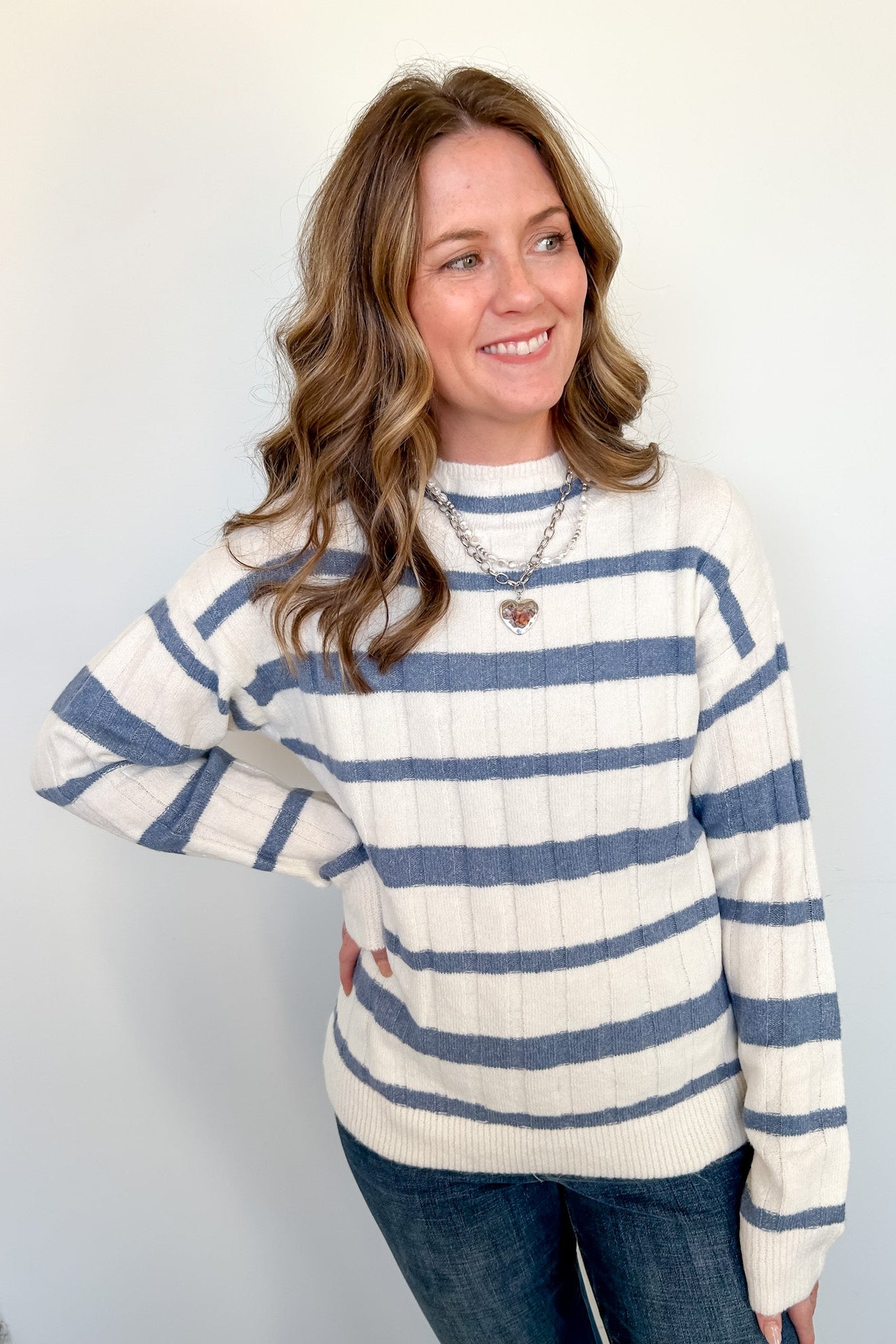 Woman in blue and white striped sweater standing against a white wall.