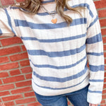 Woman in white and blue striped sweater with her arm up to her face.