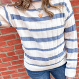 Woman in white and blue striped sweater with her arm up to her face.