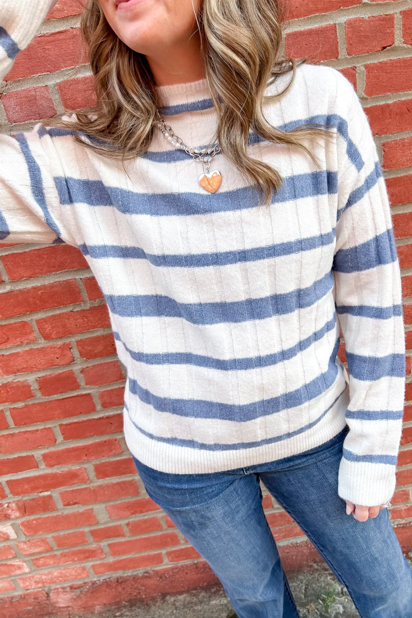 Woman in white and blue striped sweater with her arm up to her face.