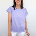 Woman wearing a light purple top with ruffled sleeves and white shorts against a plain background