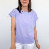 Woman wearing a light purple top with ruffled sleeves and white shorts against a plain background