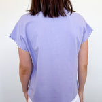 Person wearing a light purple top and white shorts against a plain background