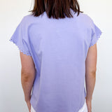 Person wearing a light purple top and white shorts against a plain background