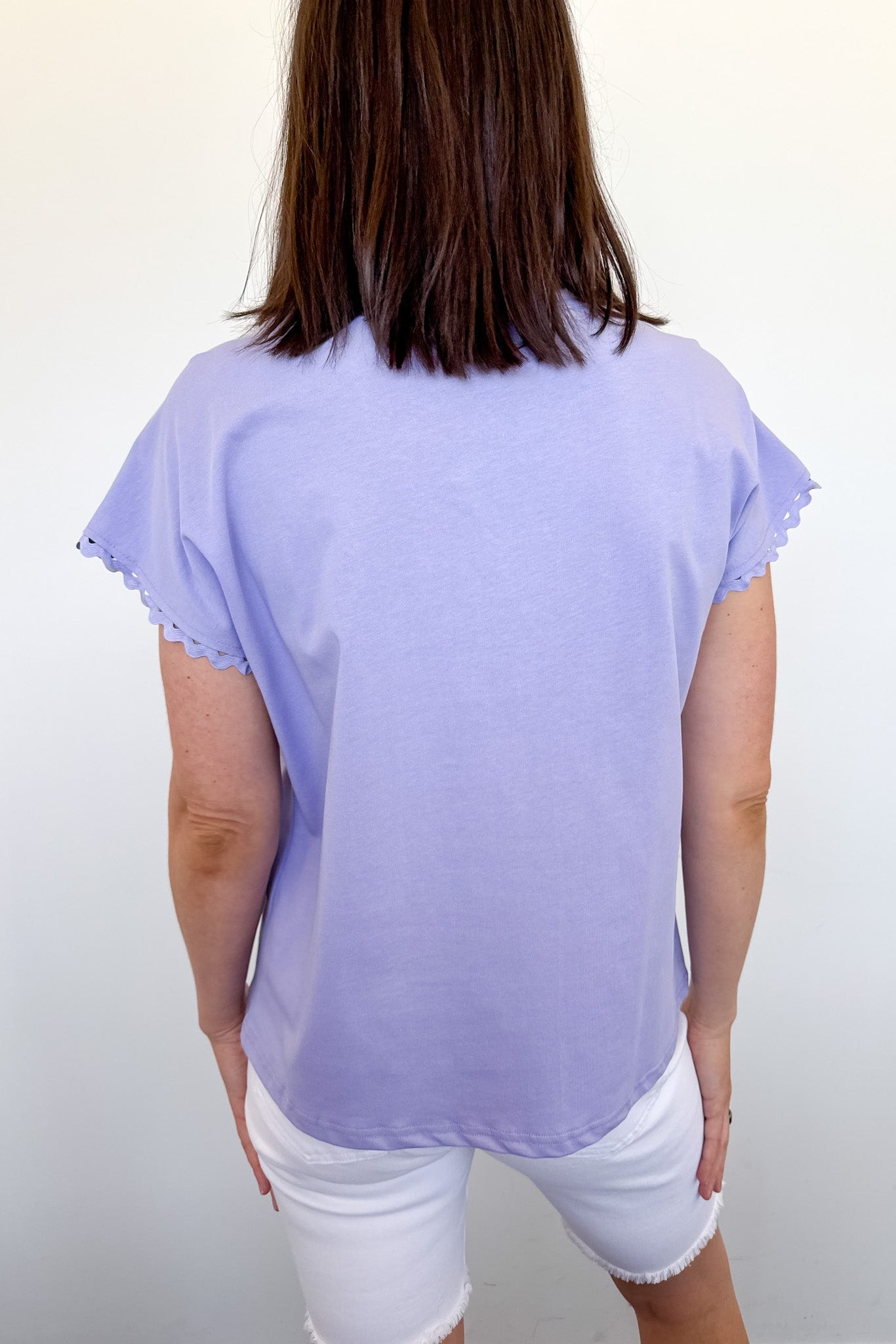 Person wearing a light purple top and white shorts against a plain background