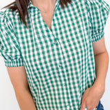Person wearing a green and white checkered shirt with blue jeans against a plain background