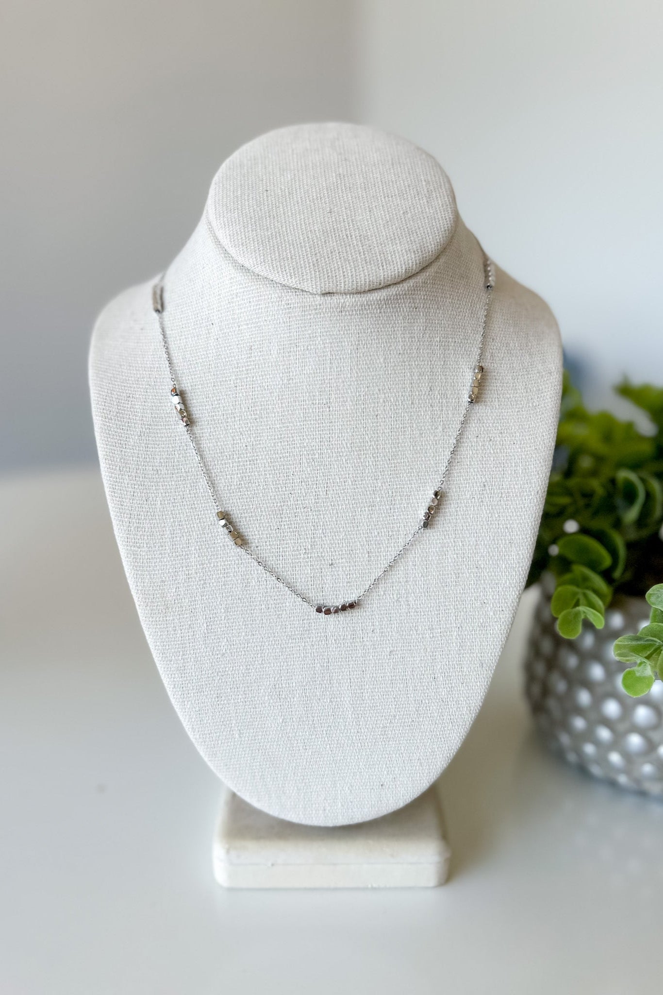 Necklace on a white bust with a plant in the background