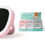 Pink handheld mirror with black surface next to a box of skincare products on a white background