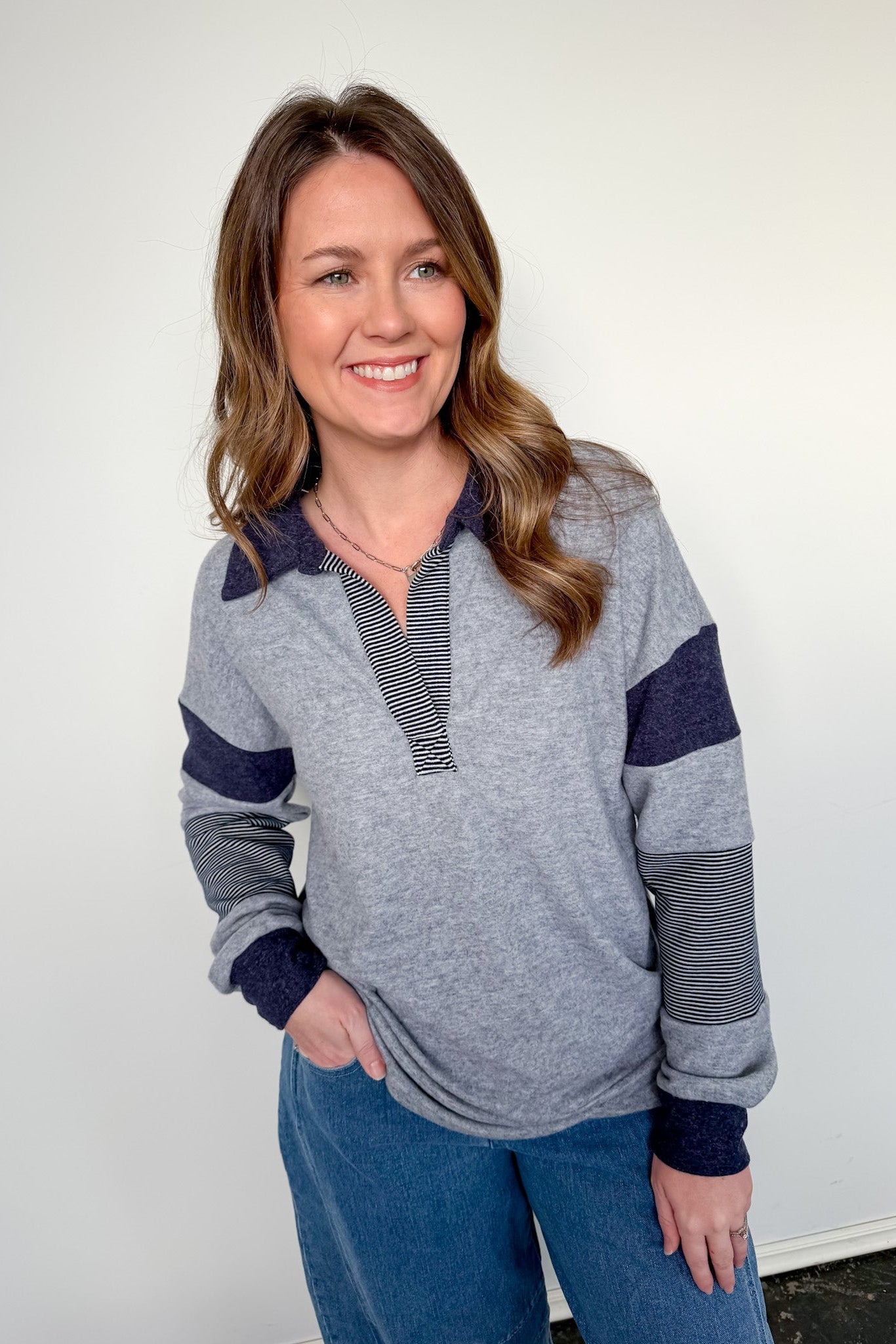 Woman wearing a gray and navy striped sweater with blue pants against a white background