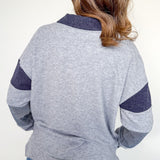 Person wearing a gray sweater with blue sleeves and collar against a white background