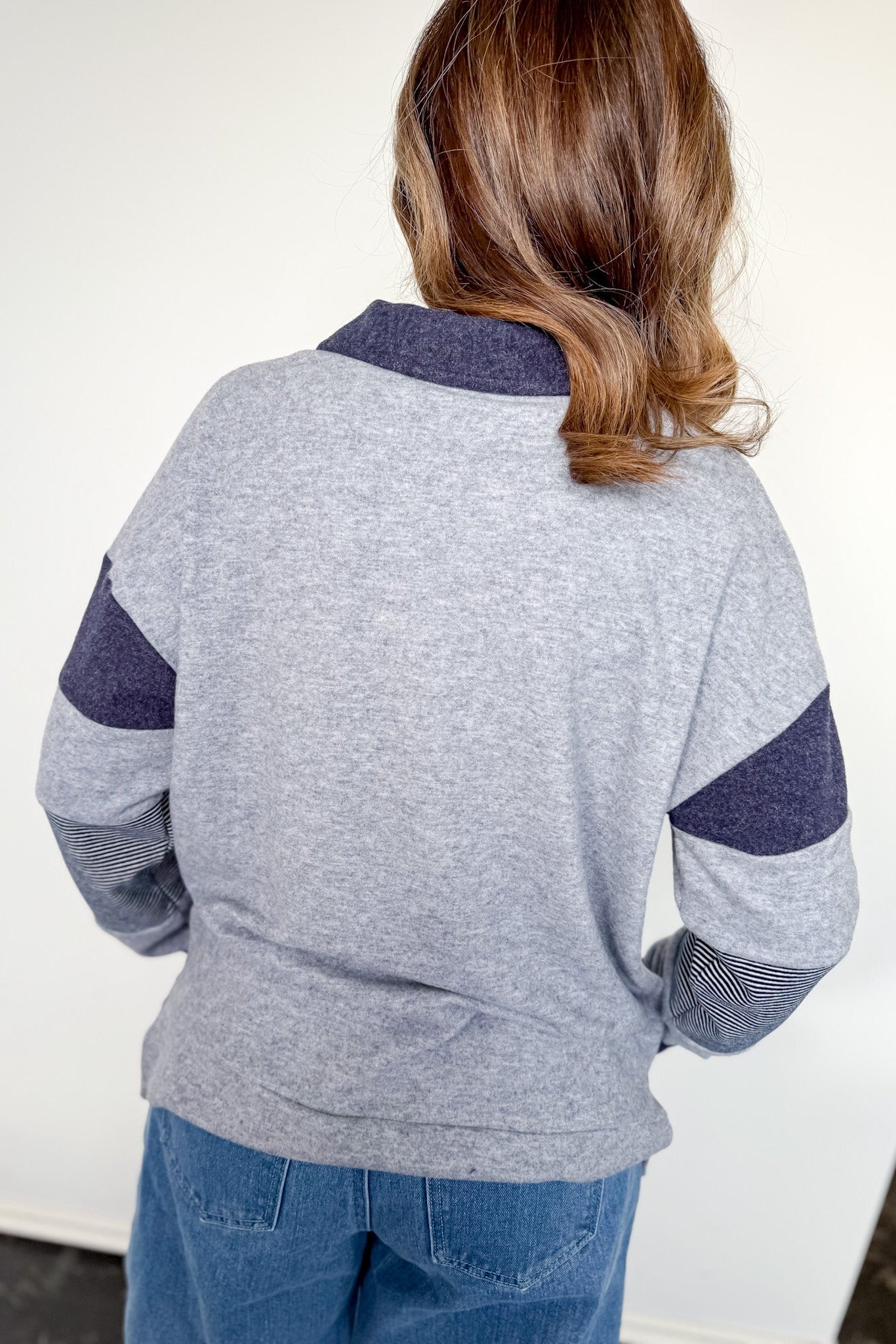 Person wearing a gray sweater with blue sleeves and collar against a white background