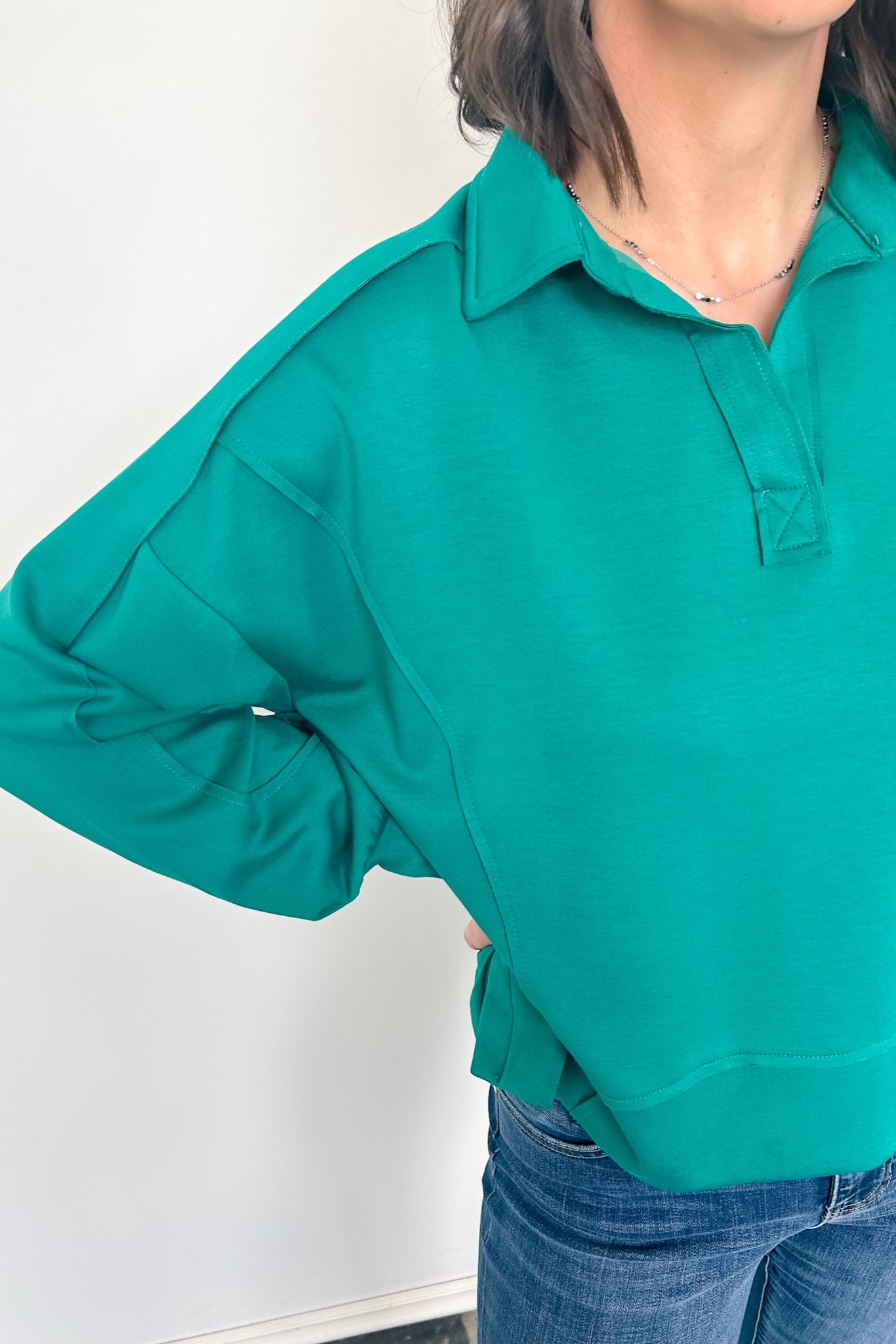 Person wearing a teal long-sleeve shirt against a white background