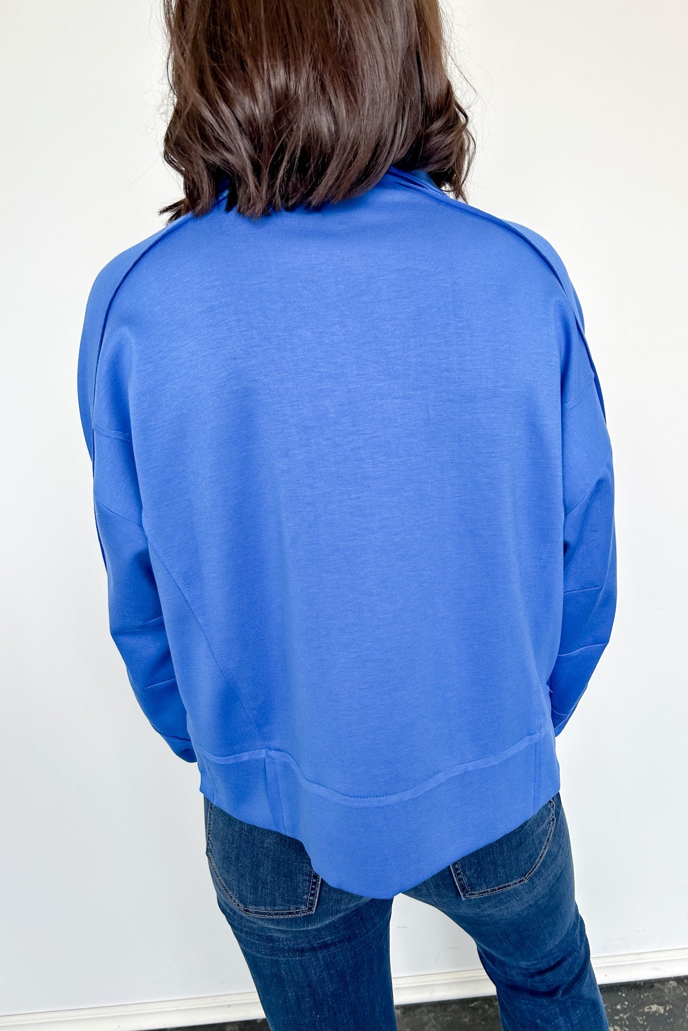 Person wearing a blue sweatshirt against a white wall