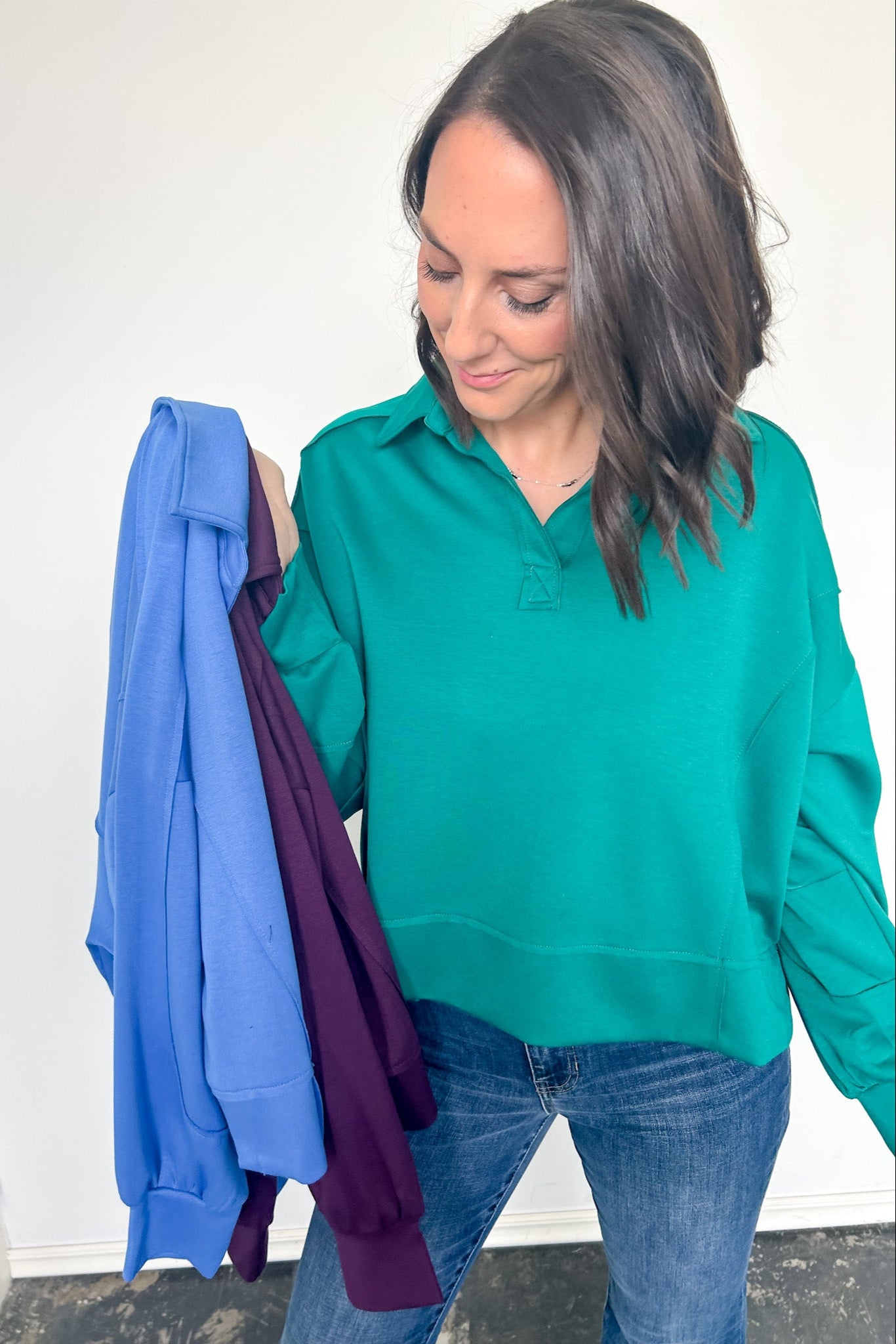 Woman holding two shirts, one blue and one purple, against a white wall.