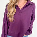 Woman wearing a purple long-sleeve top and blue jeans against a white background