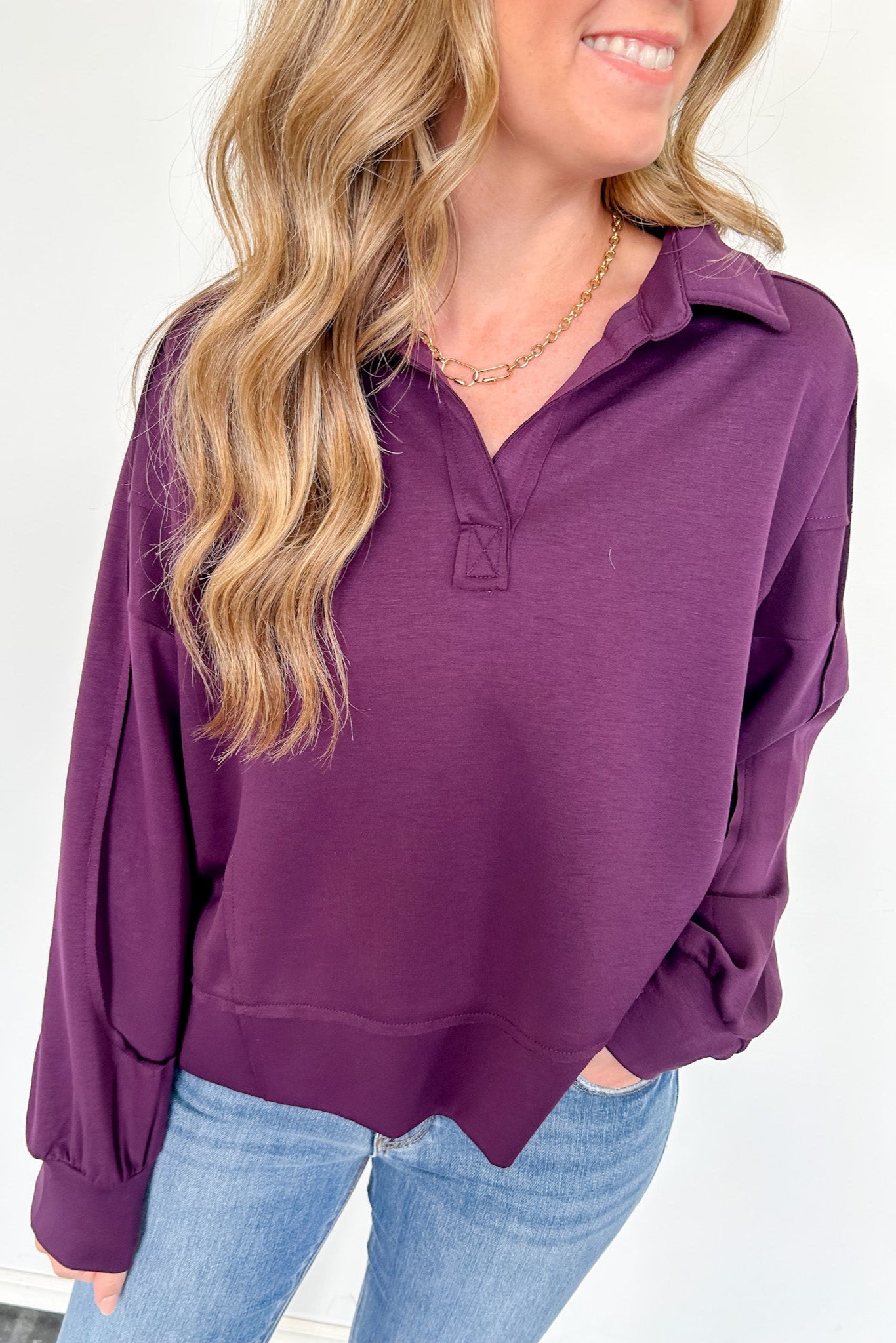 Woman wearing a purple long-sleeve top and blue jeans against a white background