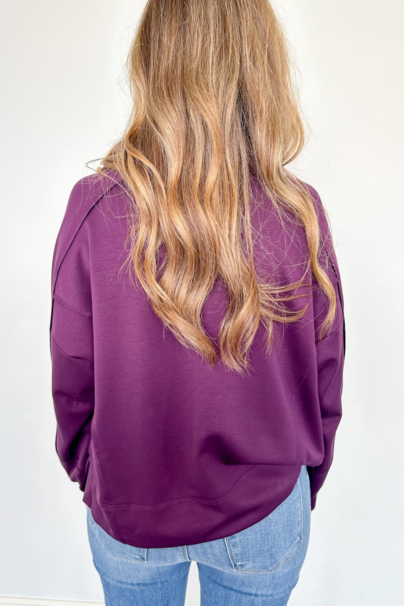 Person wearing a purple jacket and blue jeans on a white background