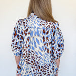 Person wearing a blue and brown patterned blouse against a white background