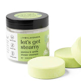 Jar of 'let's get steamy' shower steamers with three green tablets on a white background